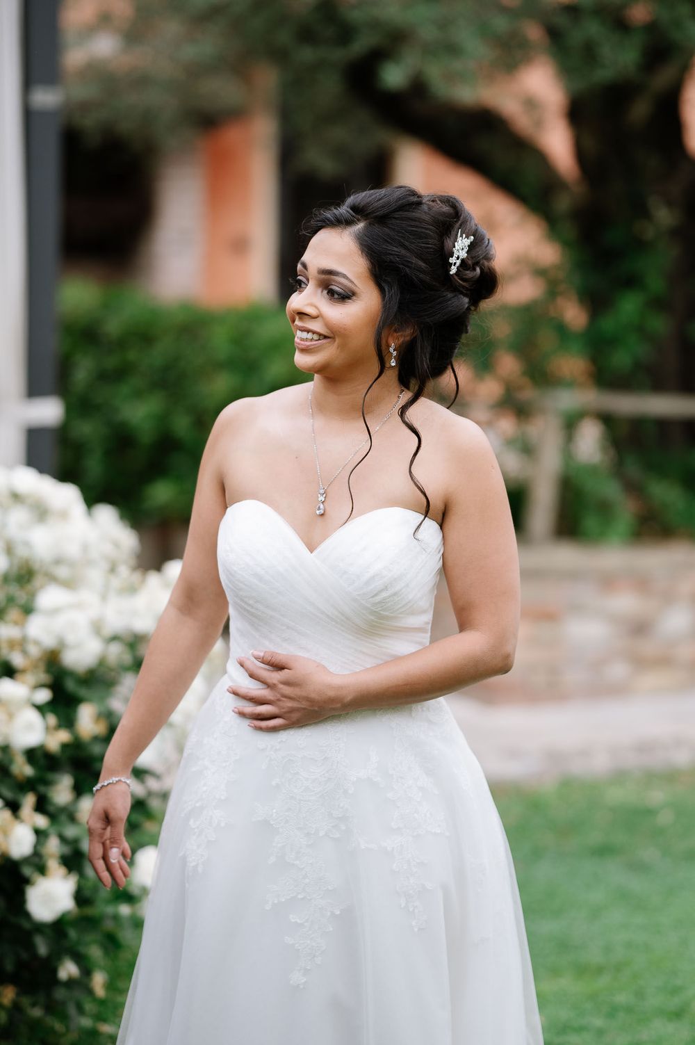 Elegant bride in a white strapless wedding gown poses in a garden setting with natural styling.