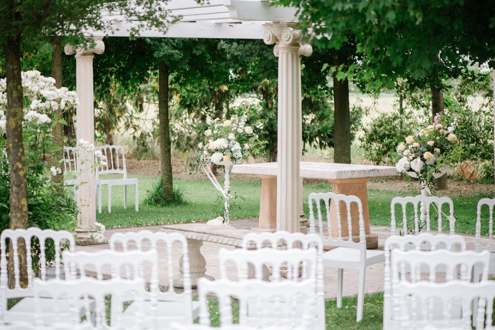 Outdoor wedding ceremony setup with white chairs and classical columns under green trees.