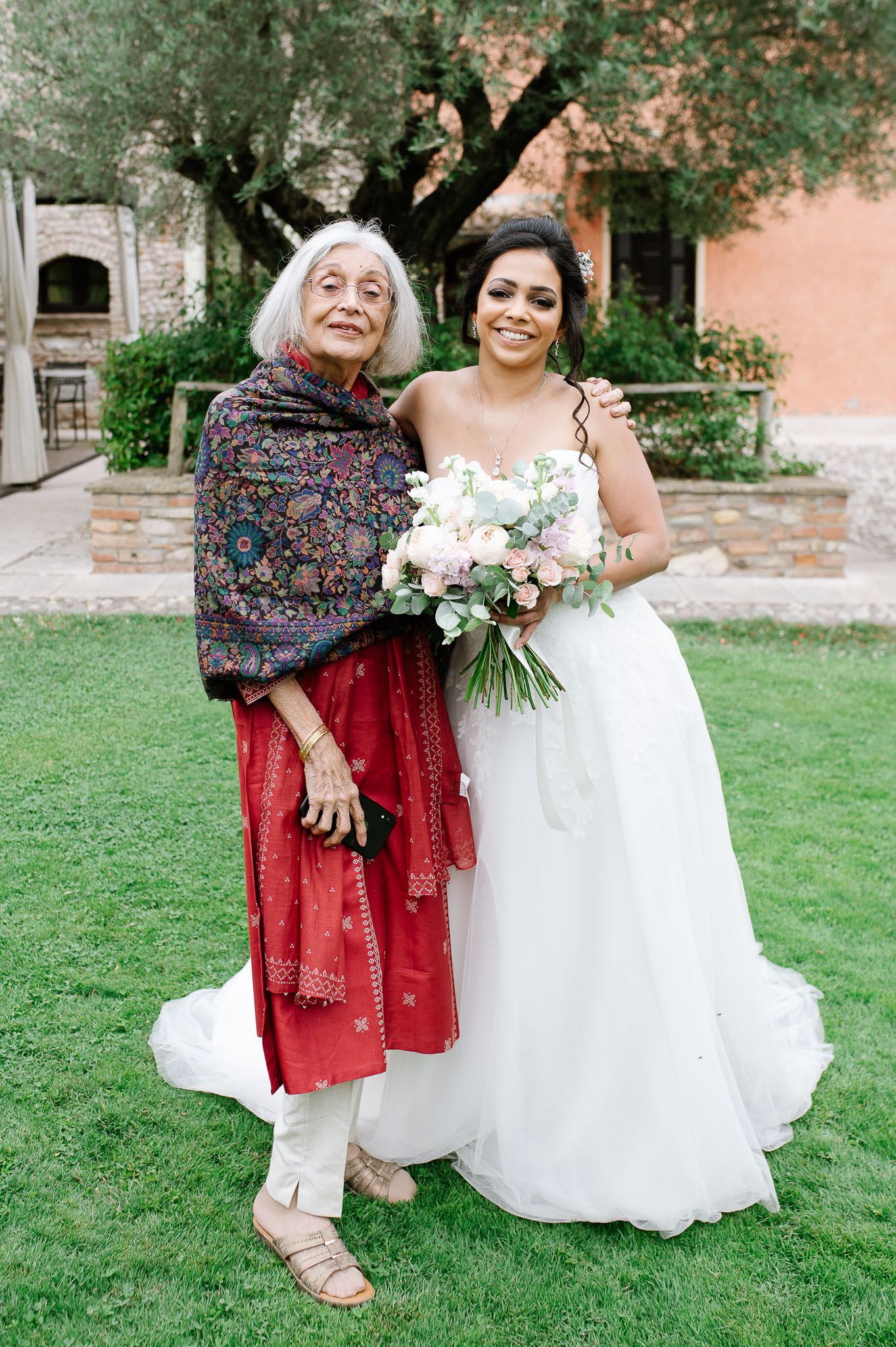 Heartwarming moment between bride in white gown and elderly woman in traditional dress.