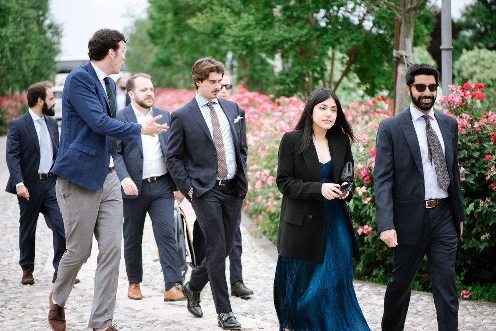 Wedding guests in formal attire walking along garden path with blooming roses.