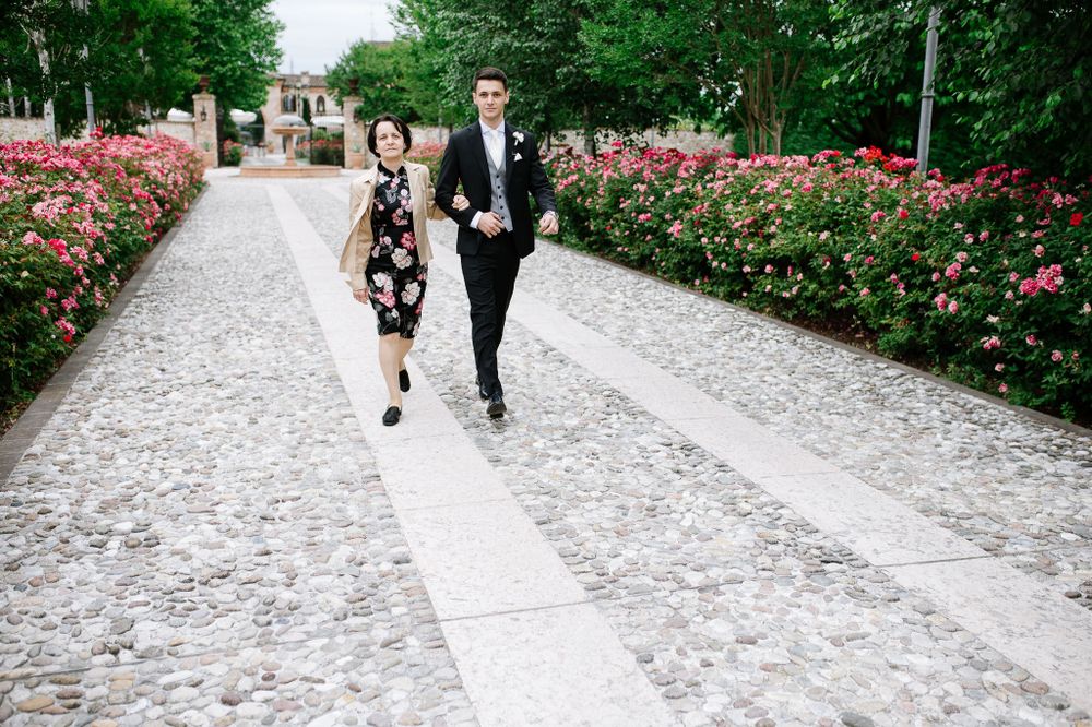A couple strolls down a rose-lined cobblestone path at an elegant outdoor venue.