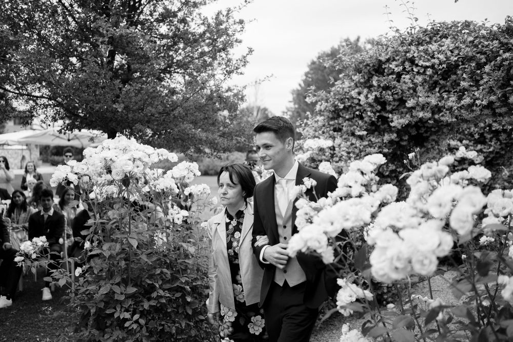 Black and white photo of person standing among blooming white flowers in a garden.