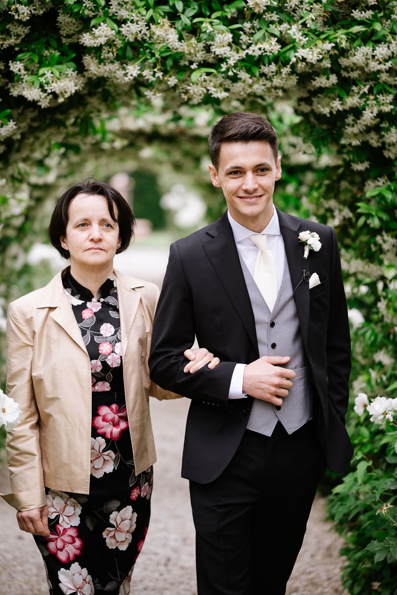 A couple poses together under flowering trees at an outdoor wedding venue.