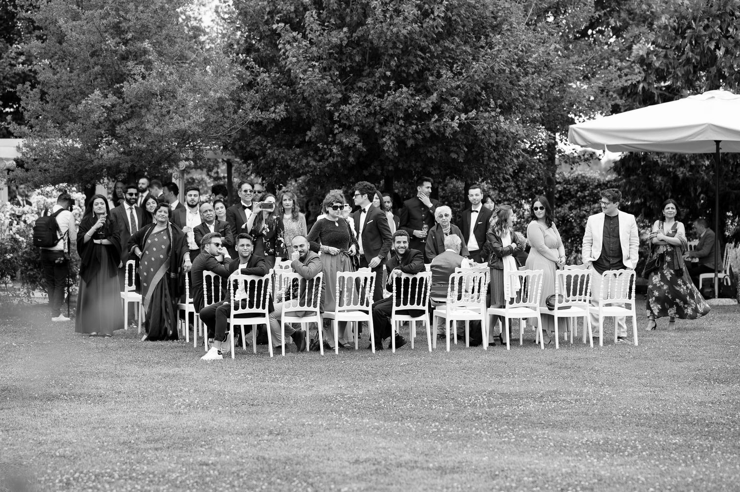 Wedding guests seated in white chairs during an outdoor garden ceremony.