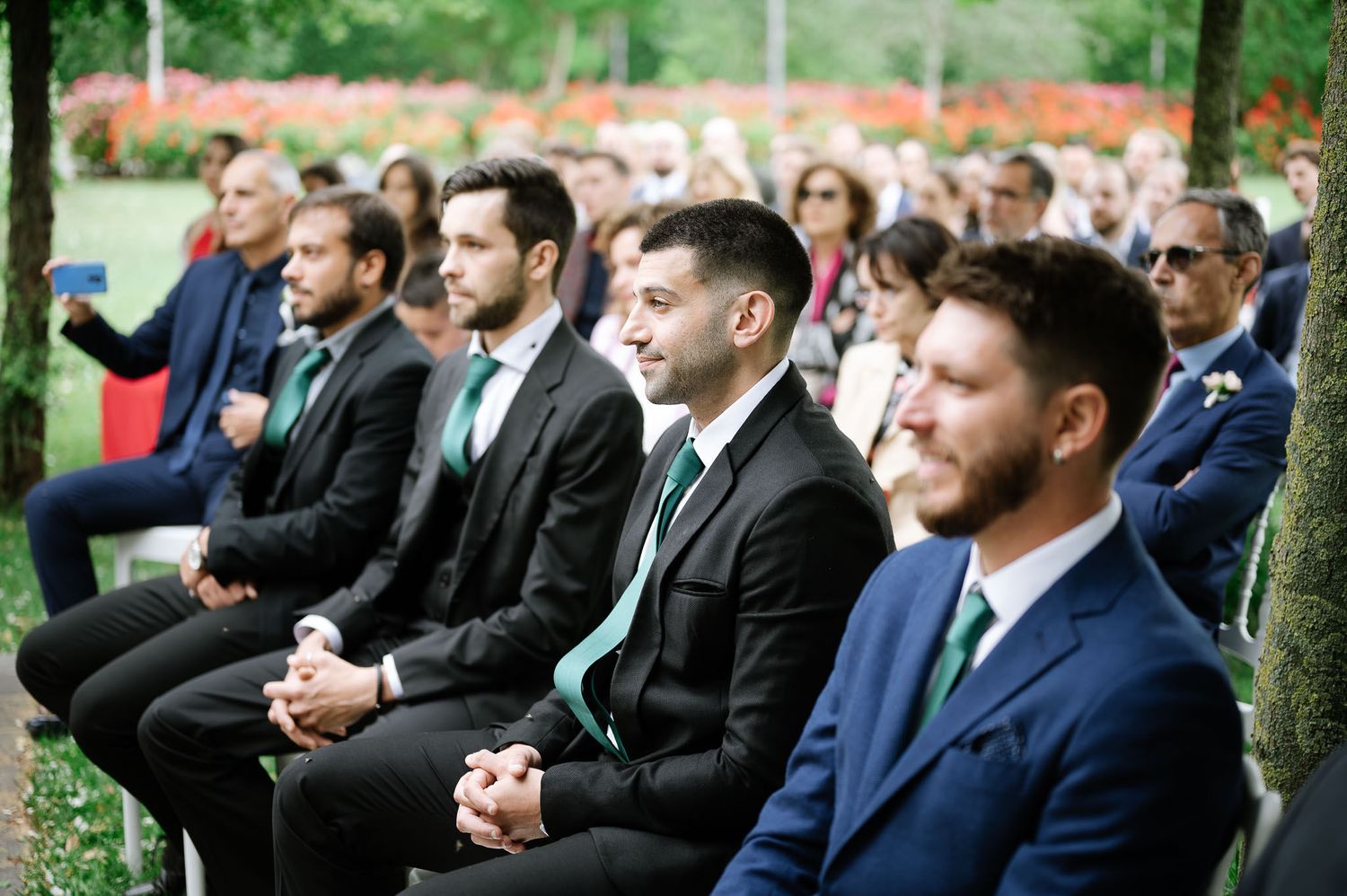 Wedding guests in formal attire seated outdoors during a garden ceremony.