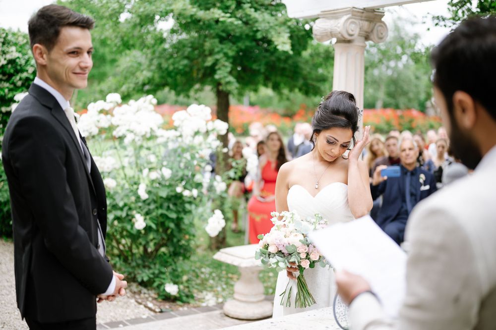 Wedding ceremony in progress under a garden pergola with guests watching.