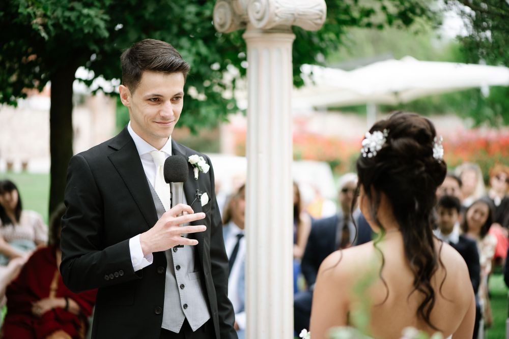 A couple shares a toast during their garden wedding ceremony under a white pergola.