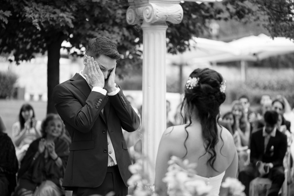 An emotional black and white moment captured during wedding vows under a garden pergola.
