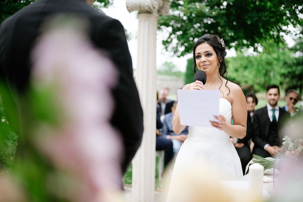 A bride reads her vows from a paper during an outdoor garden wedding ceremony.