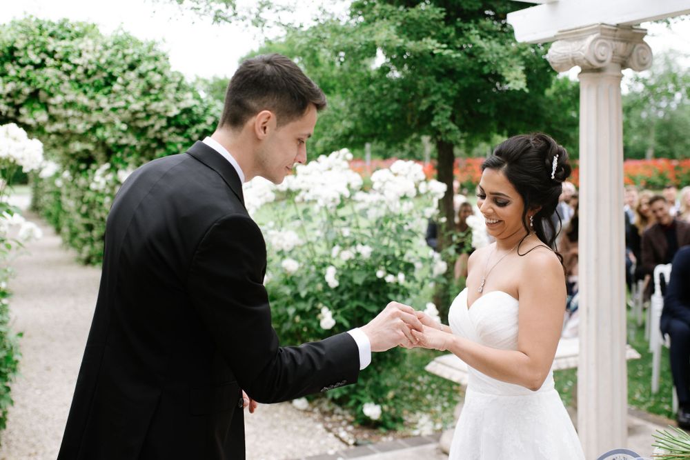 A couple exchanges rings during their wedding ceremony in a blooming garden setting.