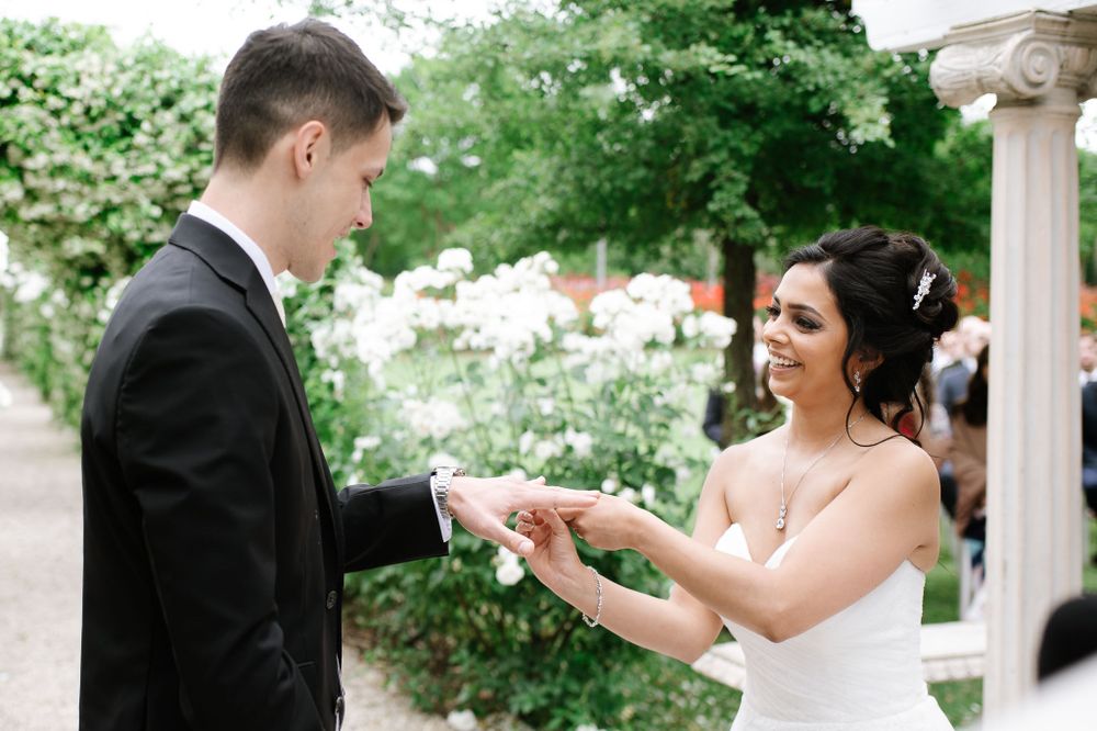 A couple exchanges wedding rings in a garden setting surrounded by blooming flowers.