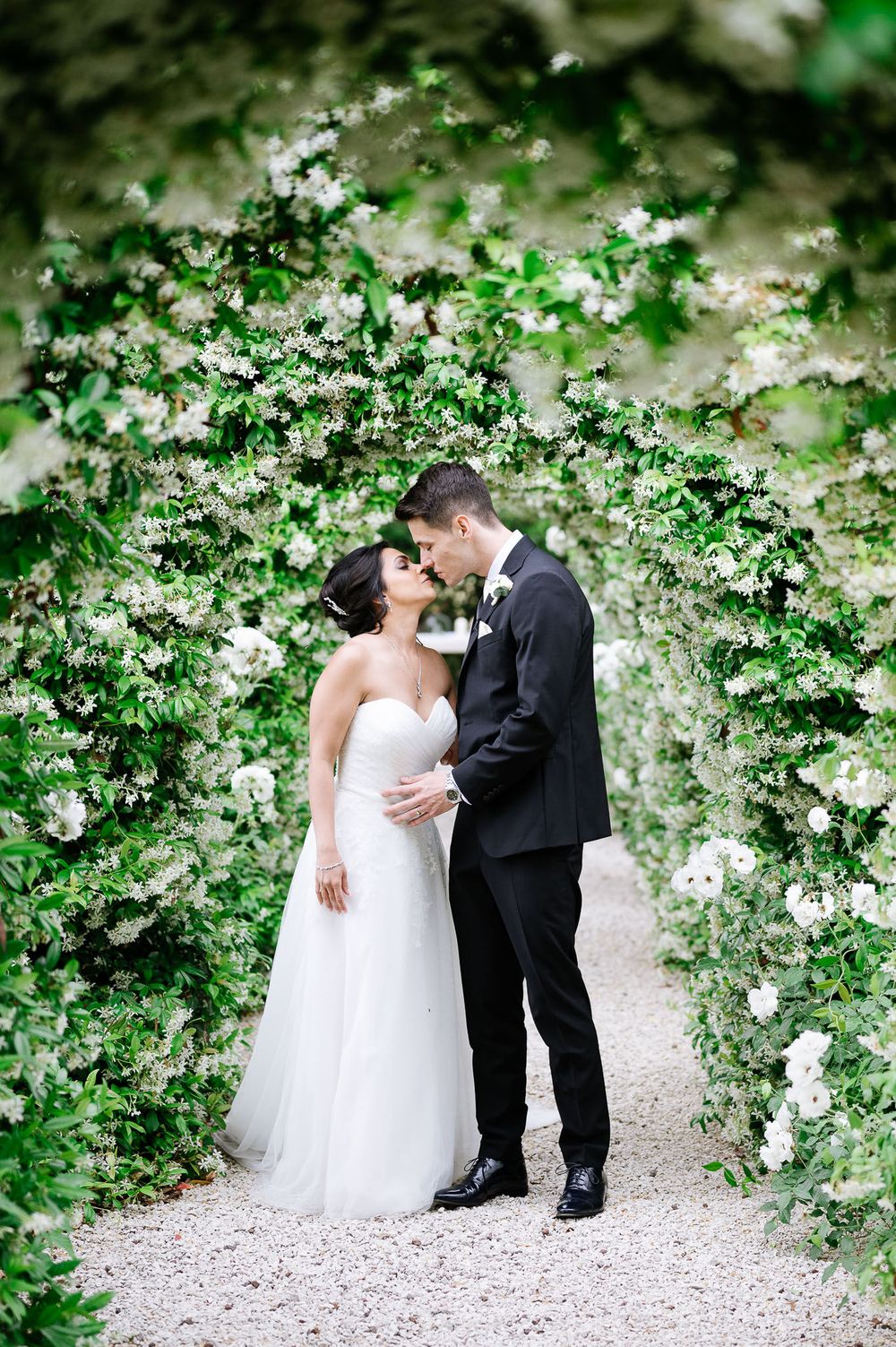 A romantic wedding moment captured under an archway of white flowering vines.
