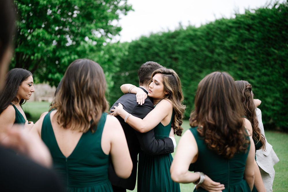 Wedding party members embrace and celebrate in an outdoor garden setting.