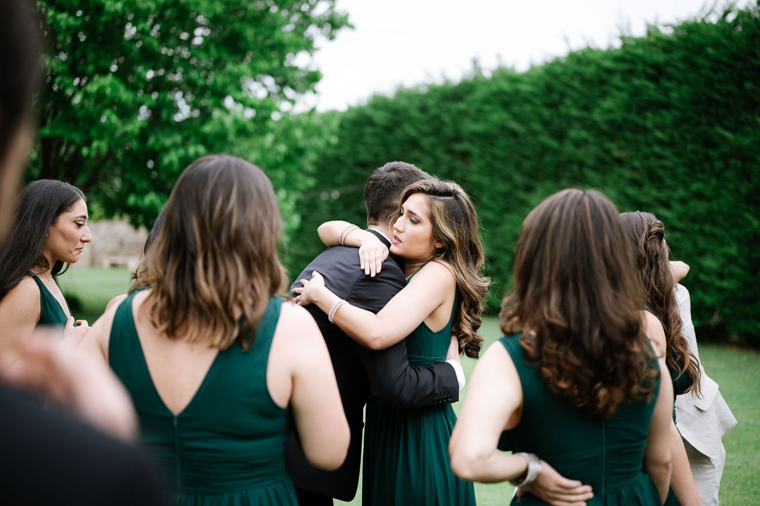 Wedding party members embrace and celebrate in an outdoor garden setting.