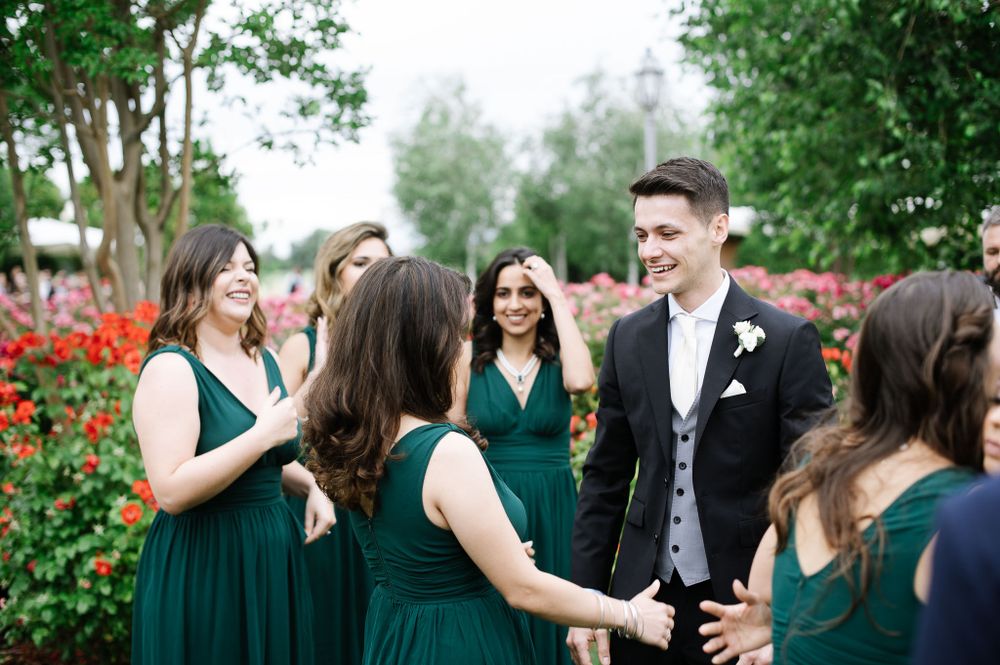 Wedding party in emerald green dresses celebrates in a garden with red flowers.