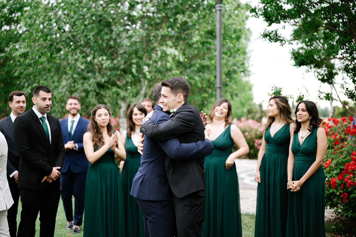 Wedding party in emerald green dresses watches celebration in garden setting.