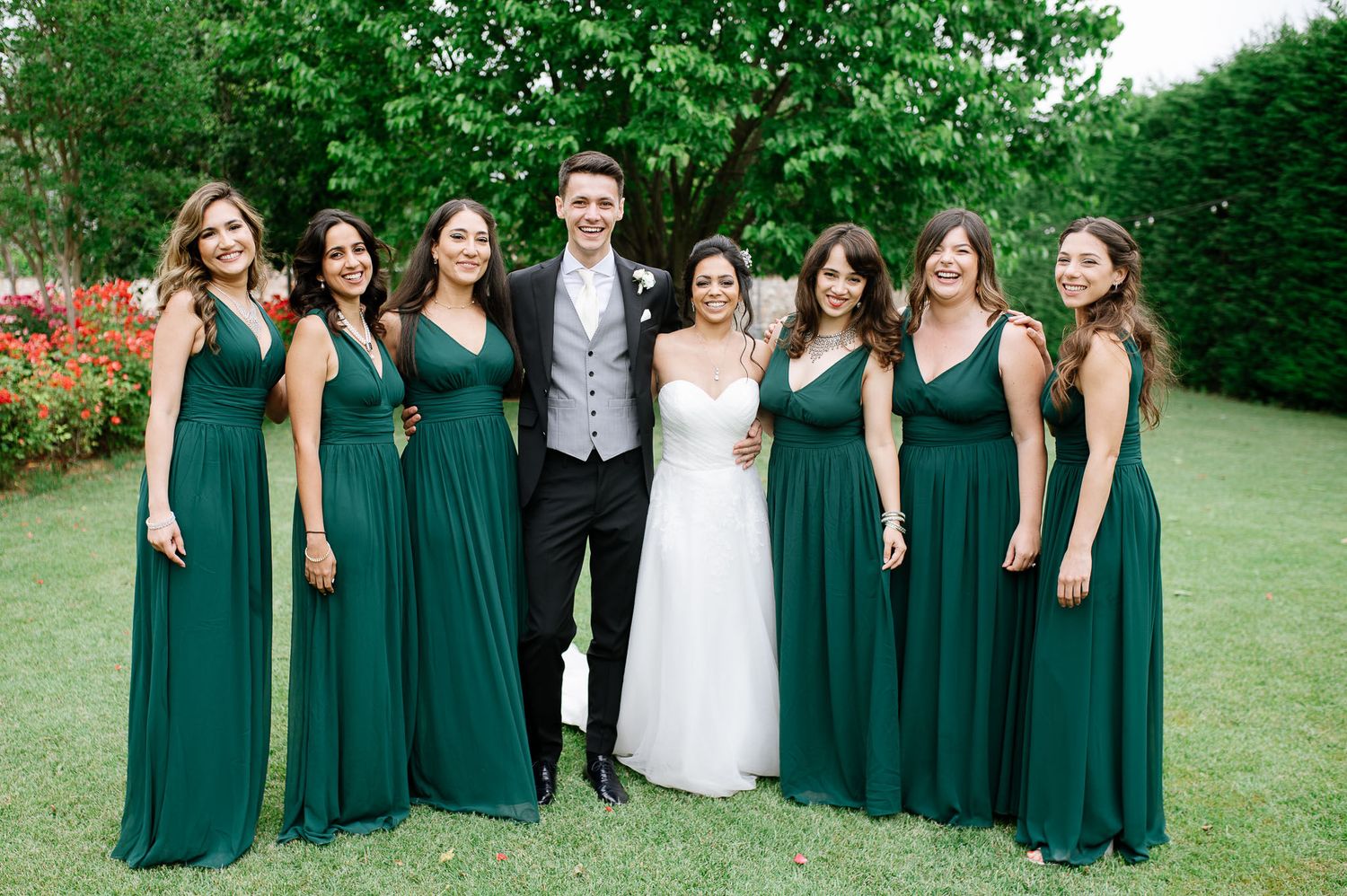Wedding party poses outdoors with bridesmaids wearing emerald green dresses.