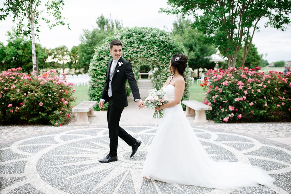 Bride and groom walking on decorative stone pathway surrounded by blooming rose gardens.
