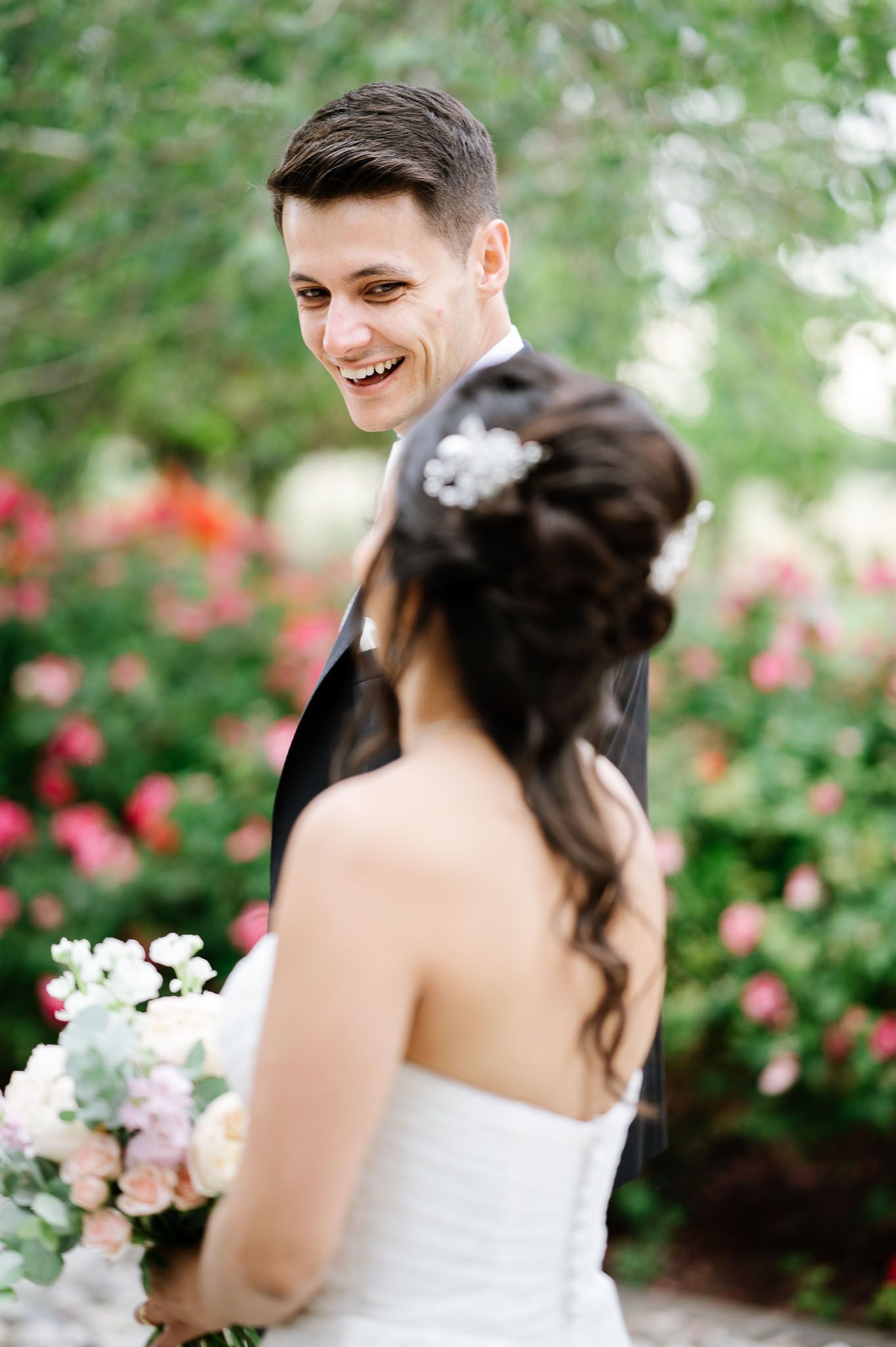 Candid moment between newlyweds surrounded by blooming roses in garden setting.