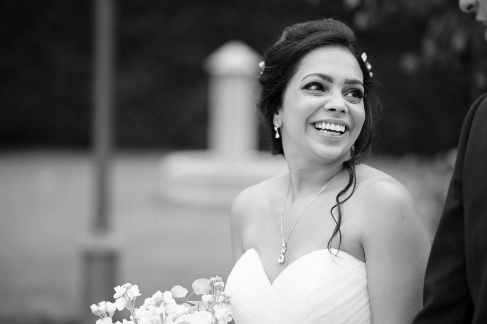 Radiant bride in strapless gown holds bouquet against black and white portrait background.