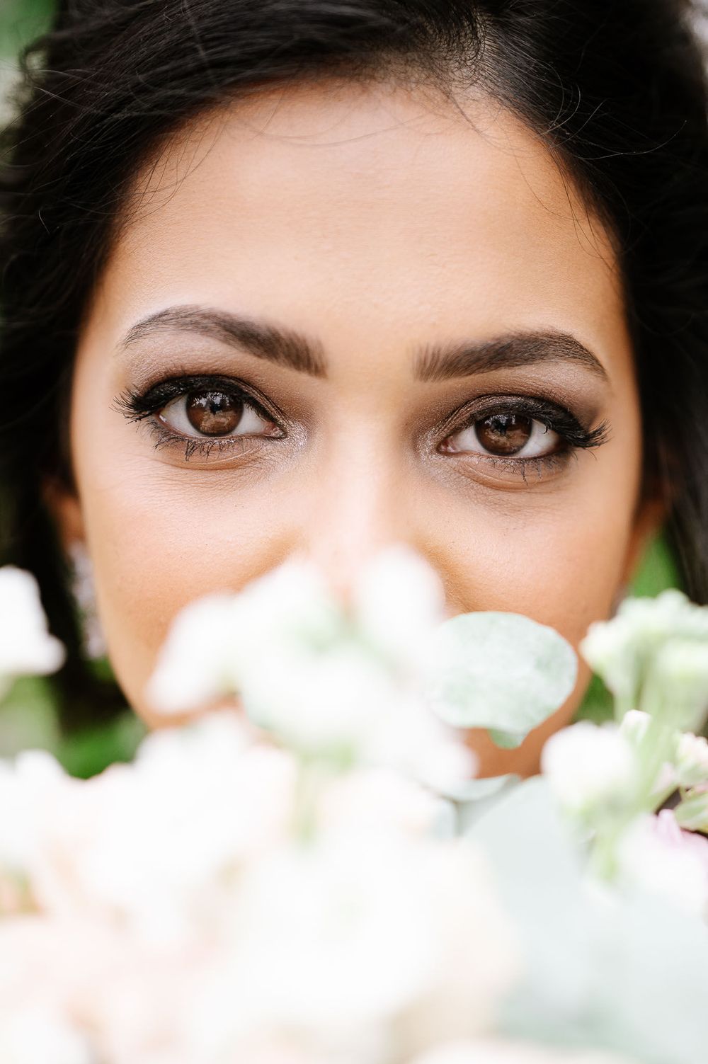 Close-up bridal portrait with white flowers softly blurred in foreground.