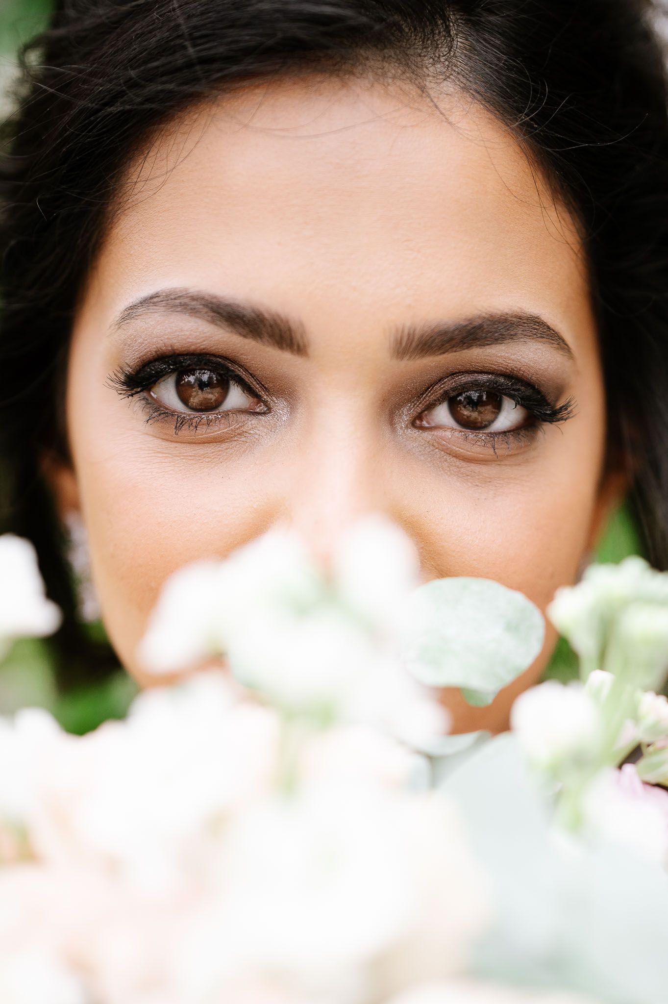 Close-up bridal portrait with white flowers softly blurred in foreground.