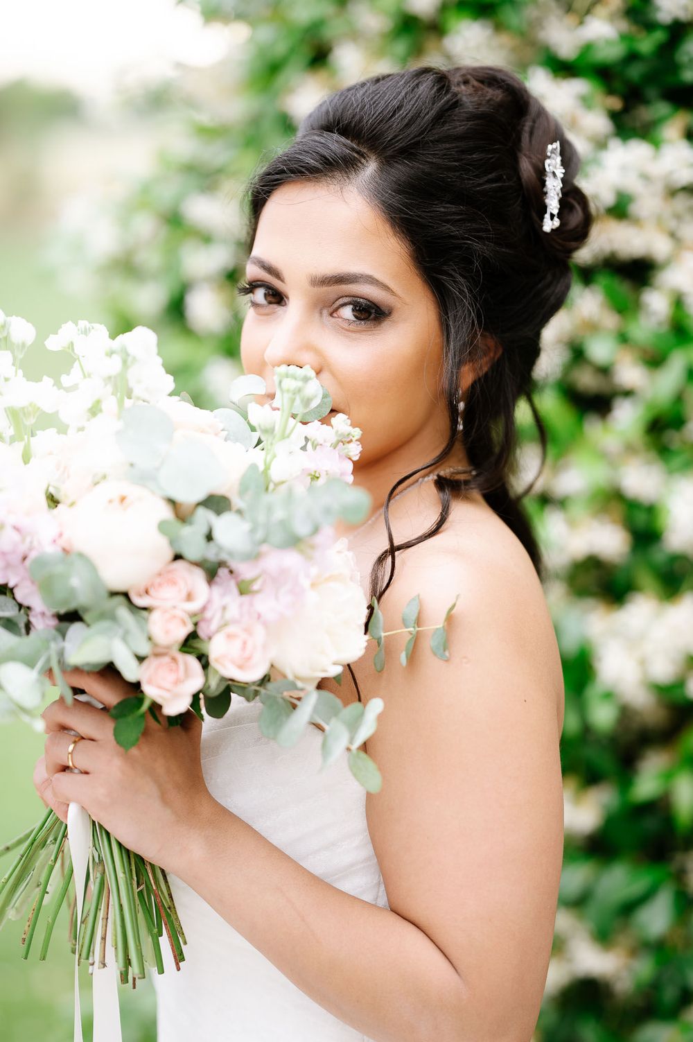 Bride holding romantic bouquet of pink and white flowers against flowering garden background.