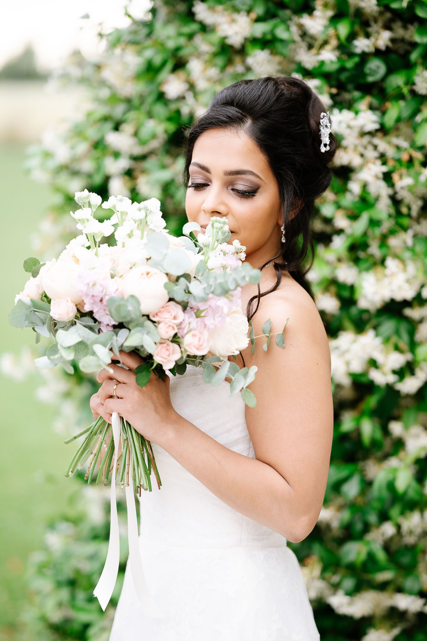 Bride smelling elegant bouquet of pink and white flowers against garden backdrop.