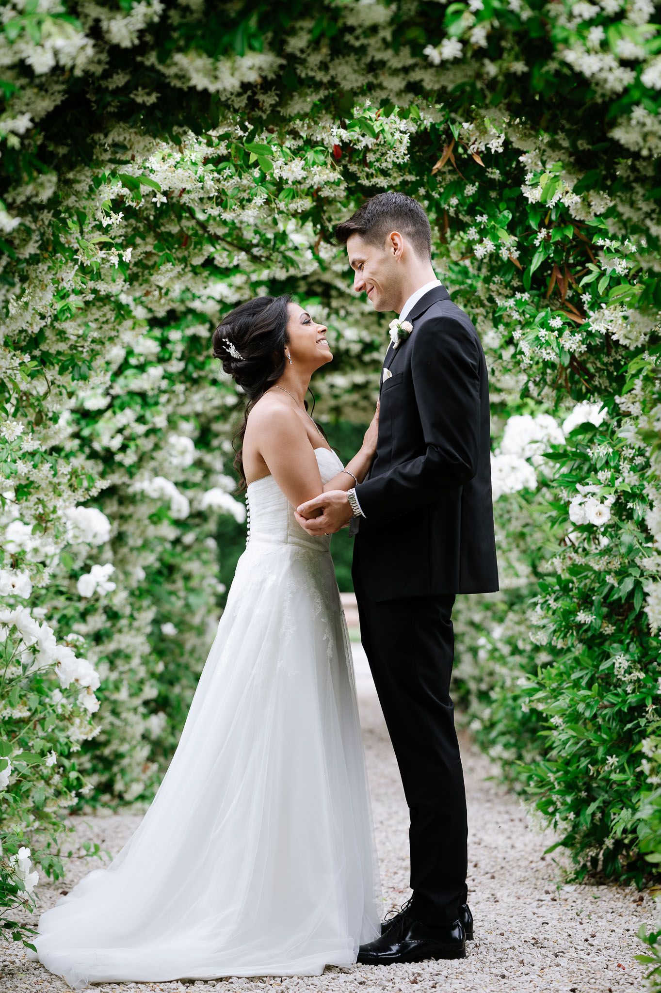 Wedding couple sharing intimate moment under canopy of white flowering vines.