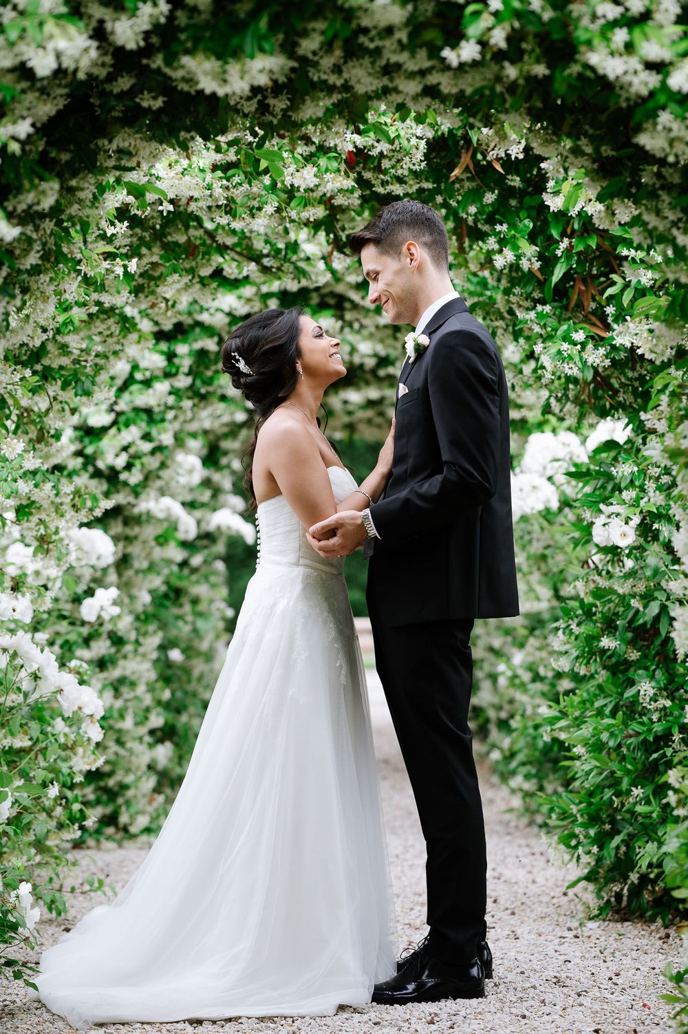 Wedding couple sharing intimate moment under canopy of white flowering vines.