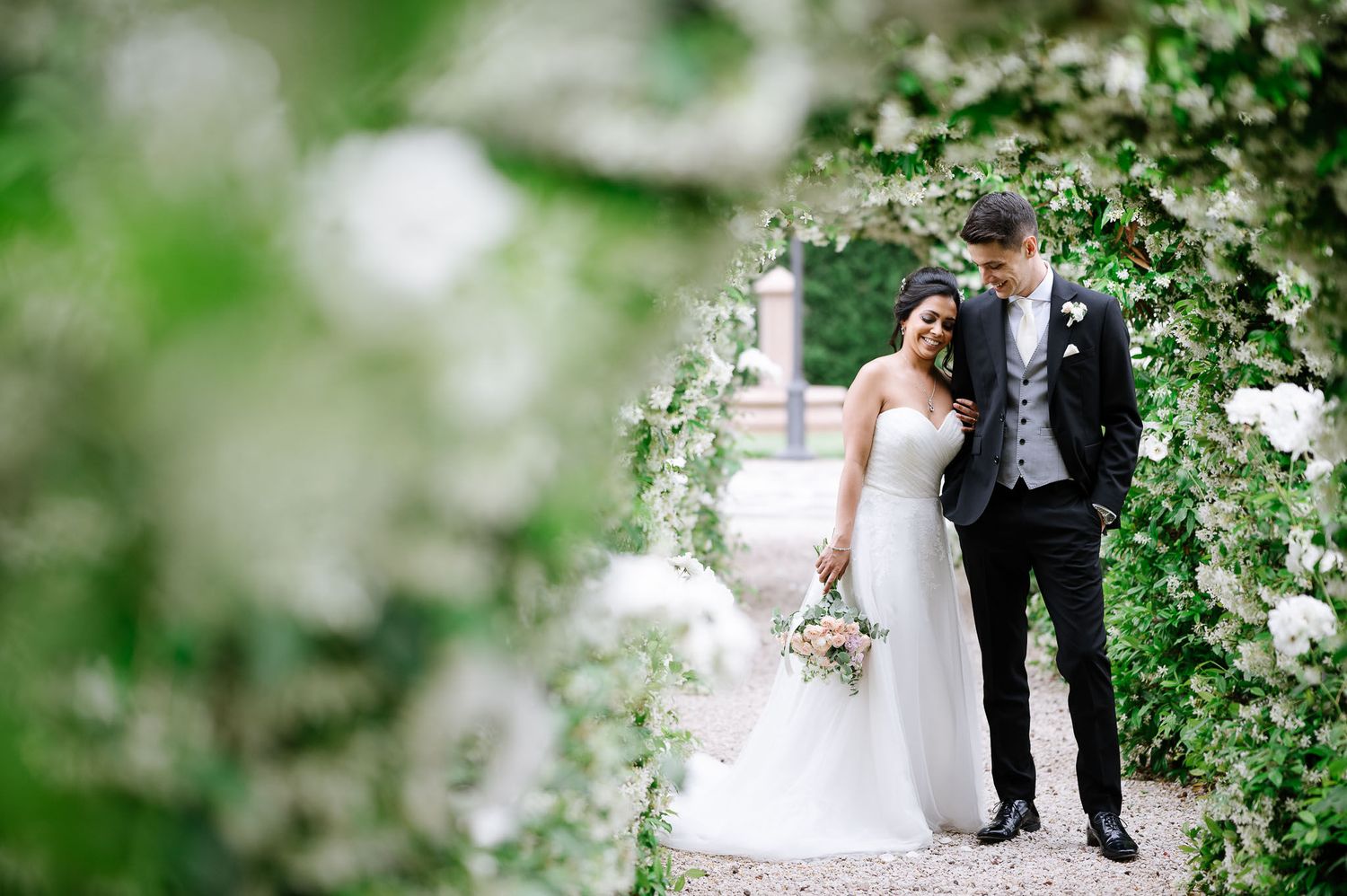 Wedding couple walking through a romantic garden pathway with white floral blooms.