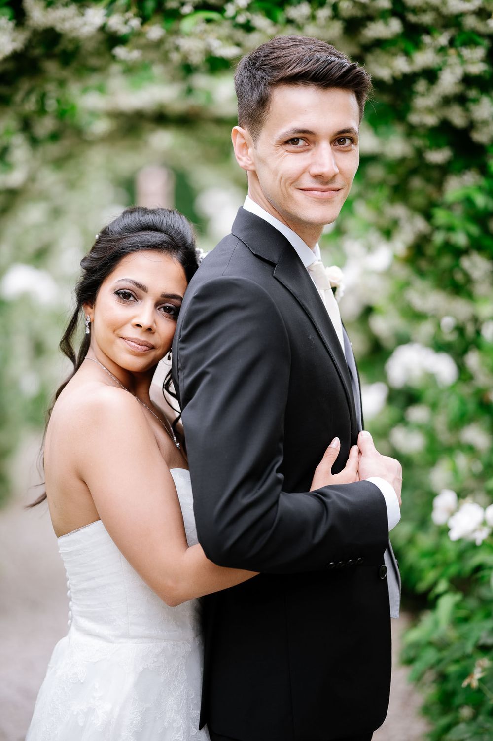 Wedding couple embracing in elegant pose against garden backdrop.
