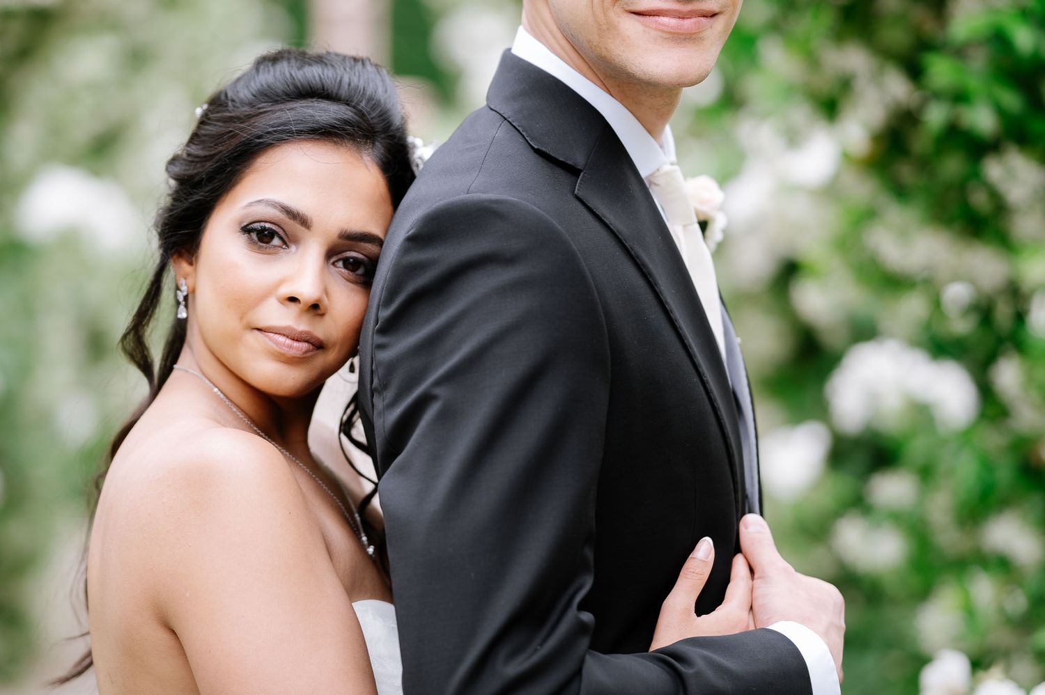 Close-up portrait of wedding couple in formal attire against garden foliage.
