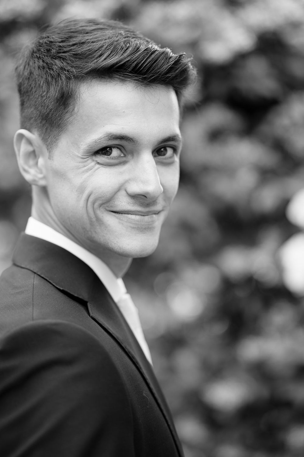 Black and white portrait of groom in classic tuxedo smiling at camera.