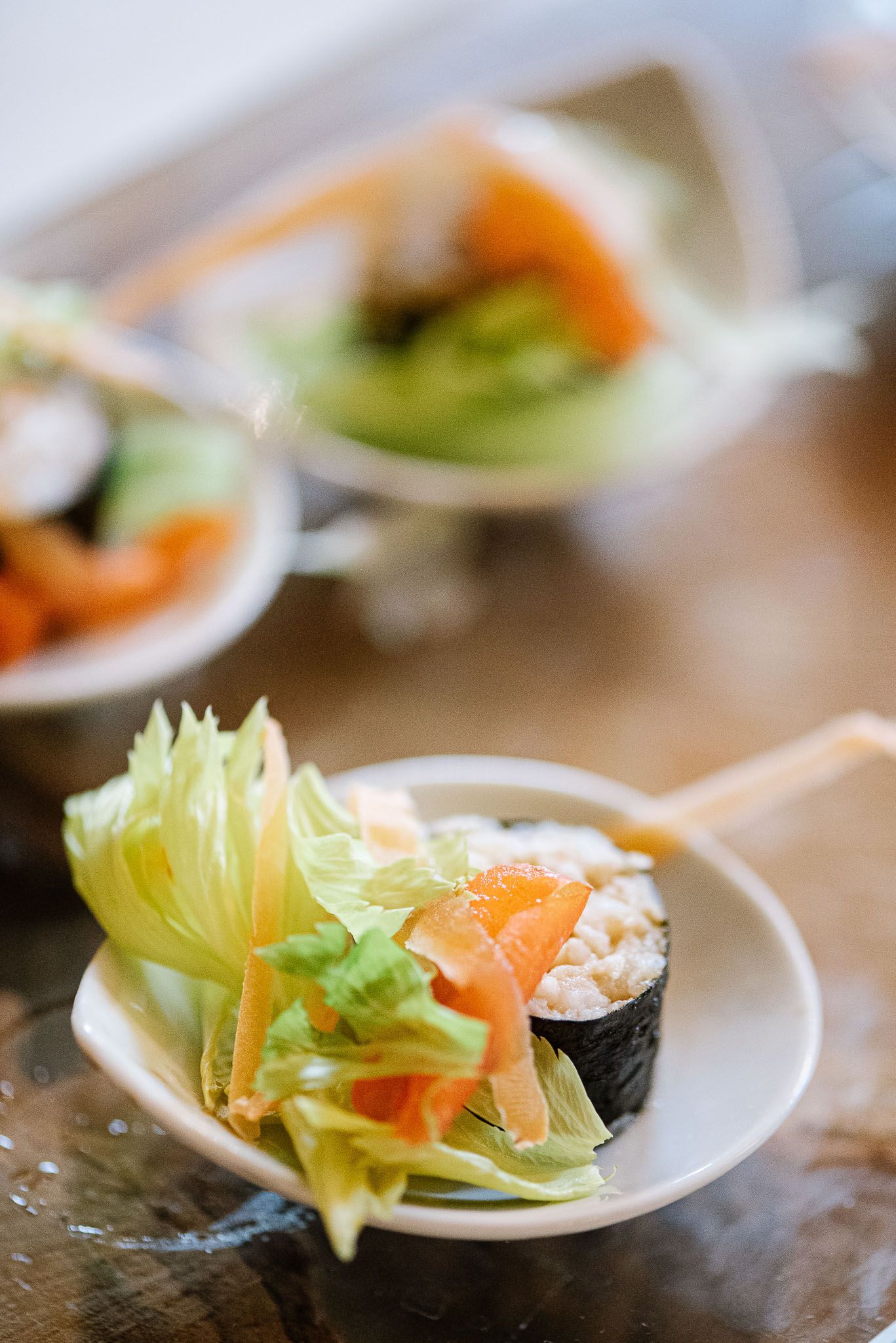 Artistic close-up of sushi garnished with fresh lettuce and carrot on a white plate.