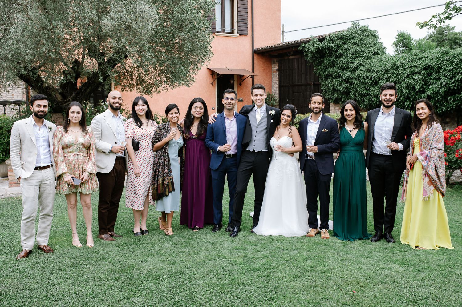 Large wedding party group photo on lawn with guests in colorful formal attire.
