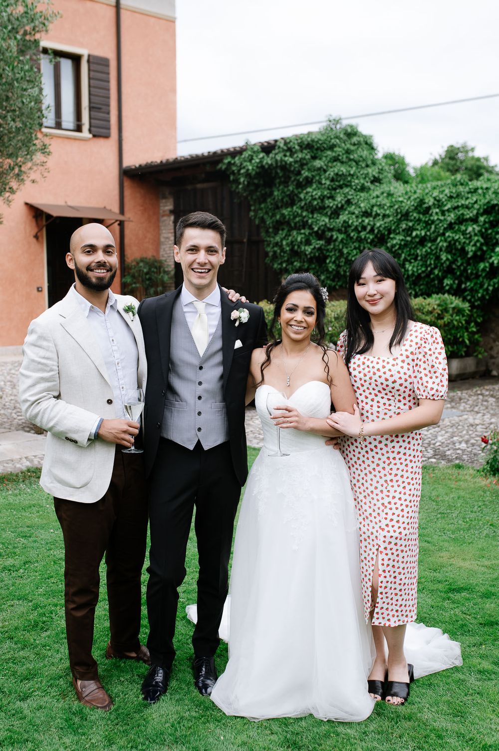 Wedding party poses on green lawn in front of terra cotta colored villa.