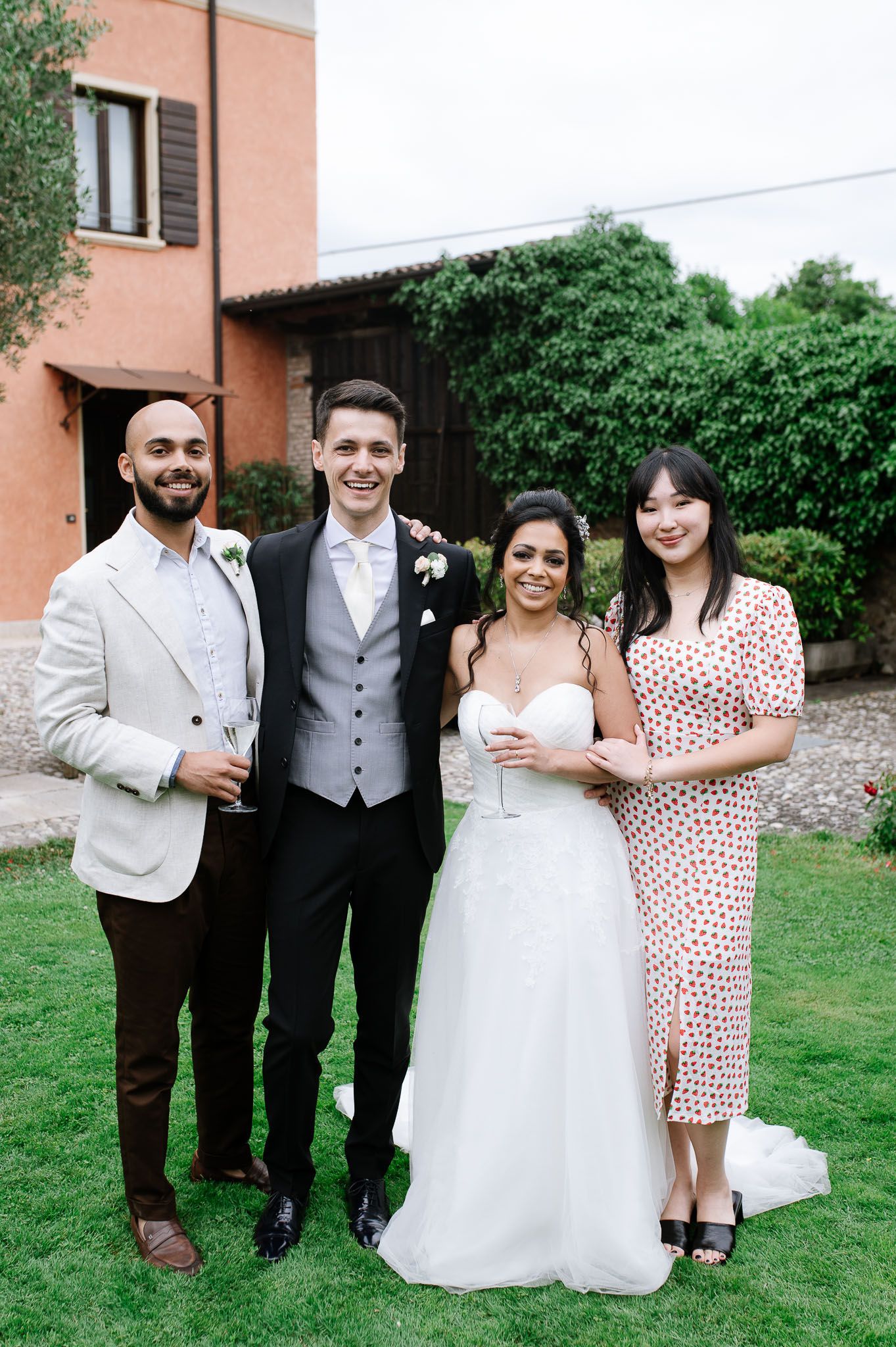 Wedding party poses on green lawn in front of terra cotta colored villa.
