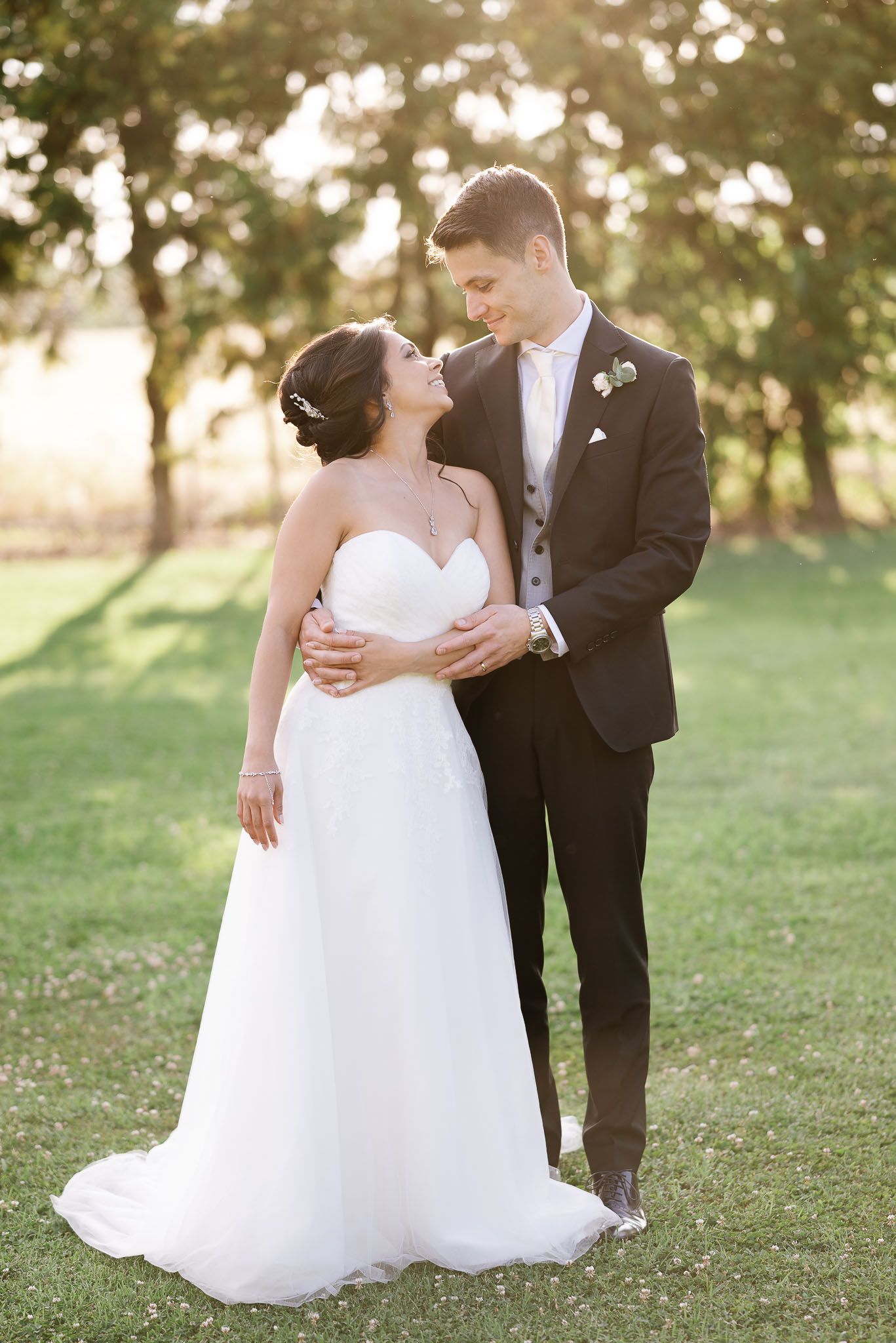 Romantic sunset portrait of newlyweds embracing on grassy lawn.