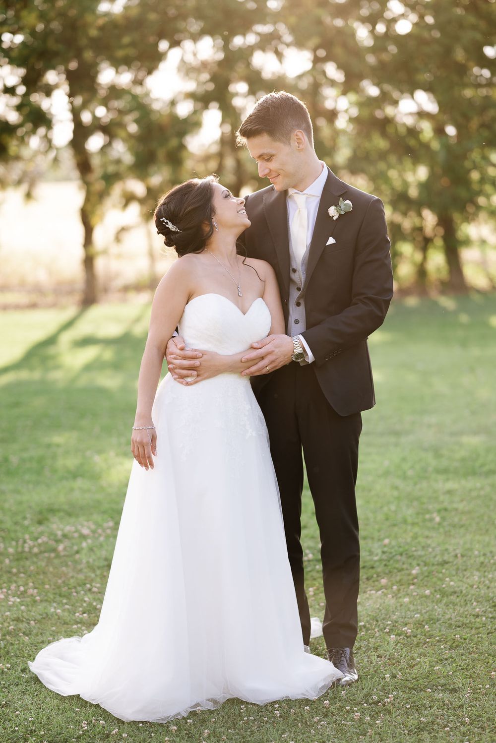 Romantic sunset portrait of newlyweds embracing on grassy lawn.