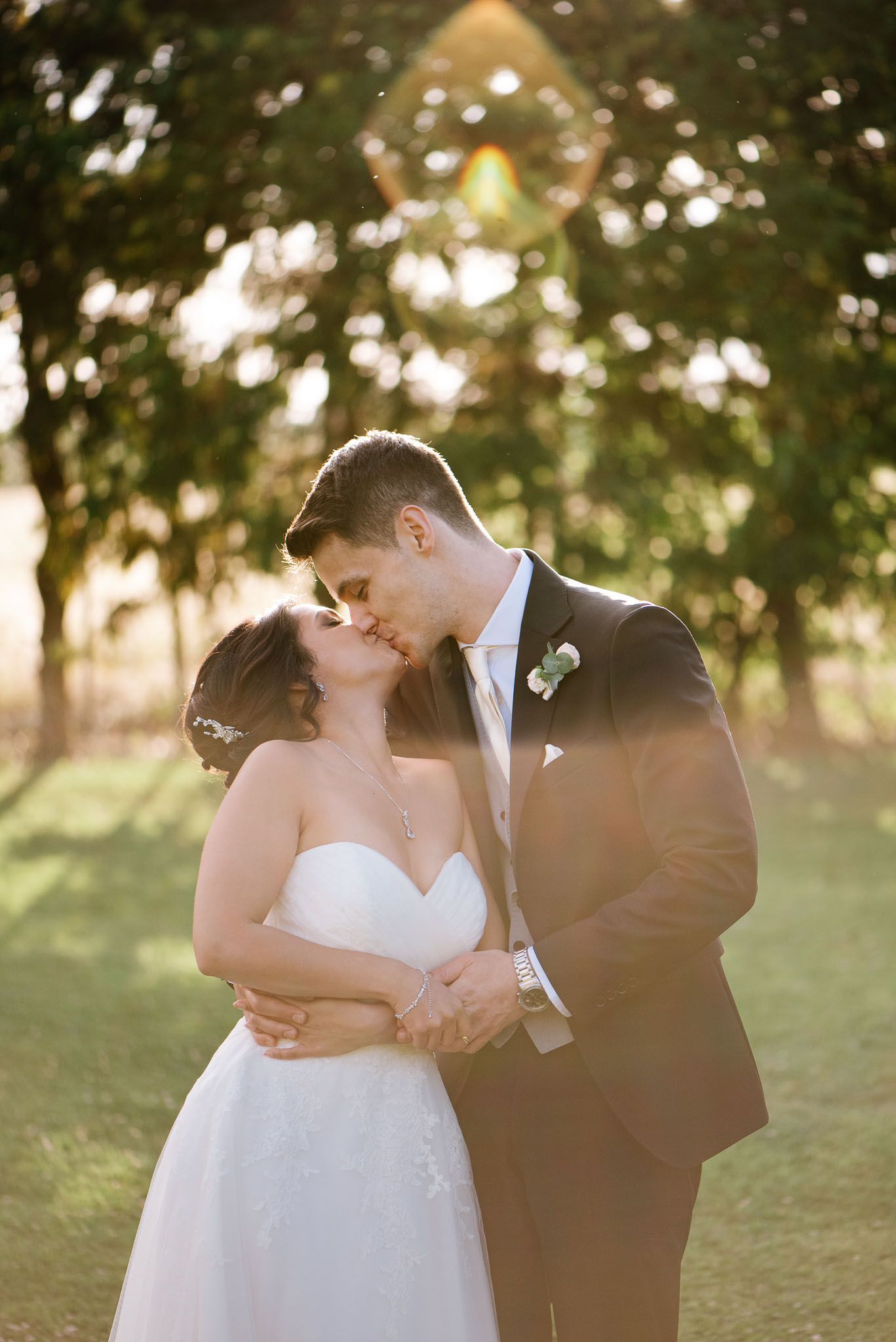 Newlyweds share tender kiss during golden hour outdoor photo session.