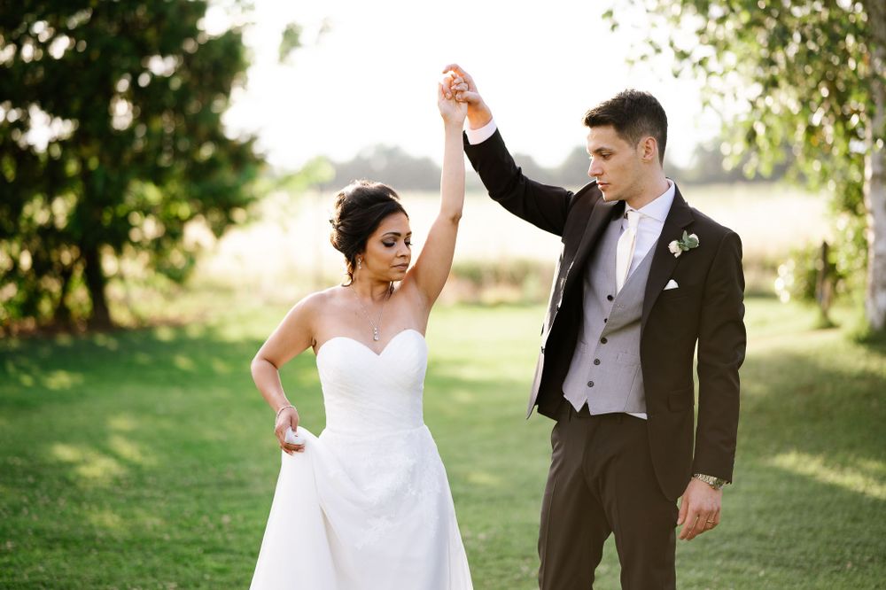 Joyful newlyweds dancing and celebrating on lawn during wedding portraits.
