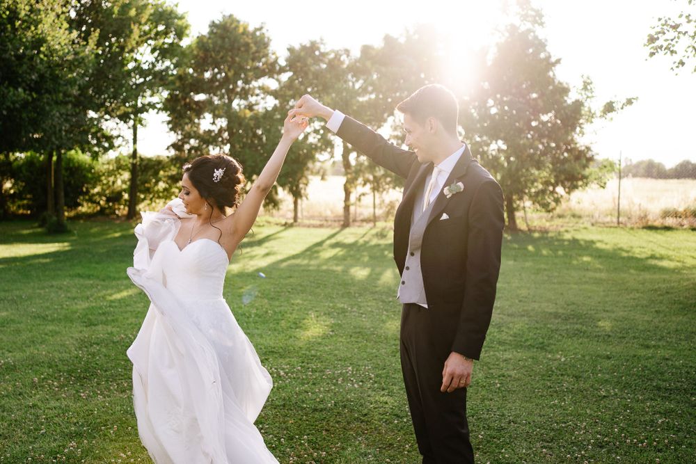 A couple dancing together outdoors during their wedding photoshoot with golden sunlight filtering through trees.