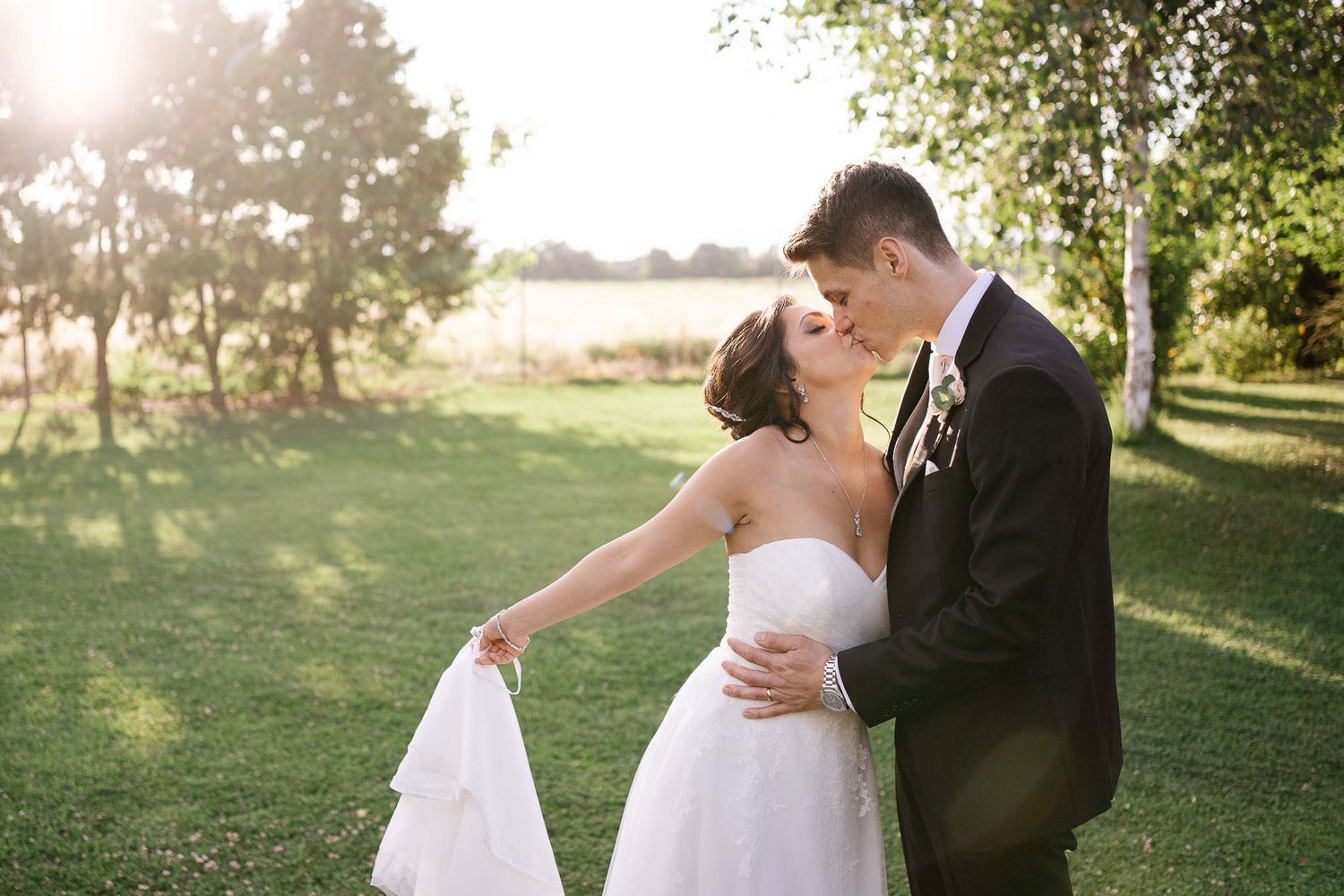 Newlyweds share a romantic moment on a grassy lawn during sunset.