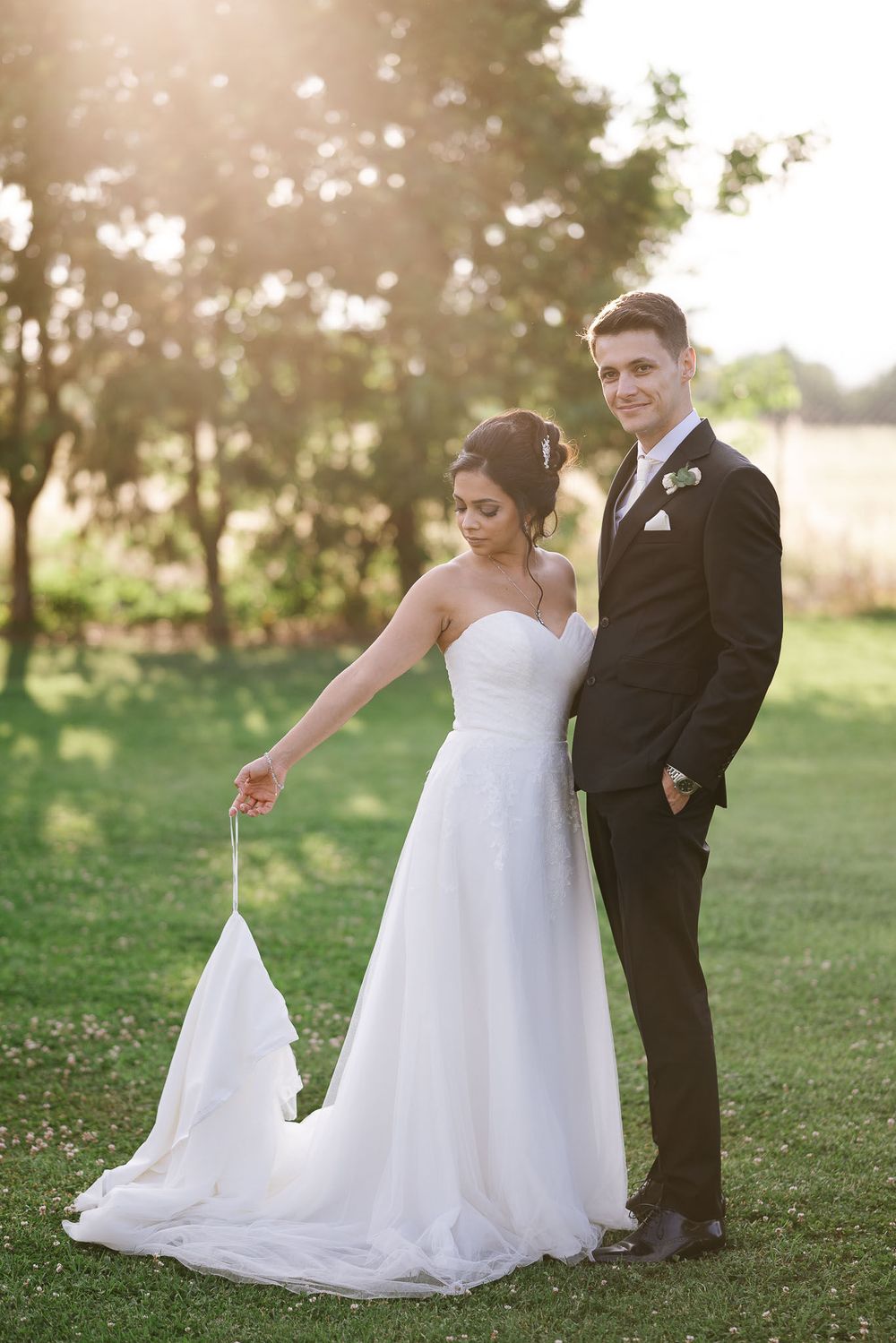 Newlywed couple poses outdoors in scenic setting with flowing white wedding dress and classic black tuxedo.