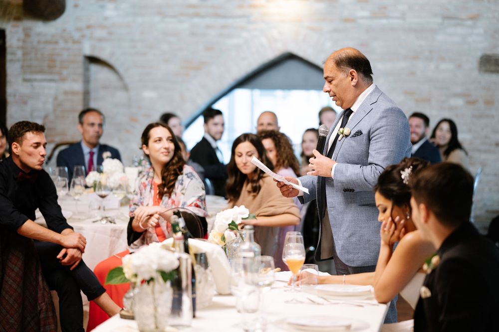 Wedding celebration in elegant brick-walled venue with guests gathered around tables during speeches.