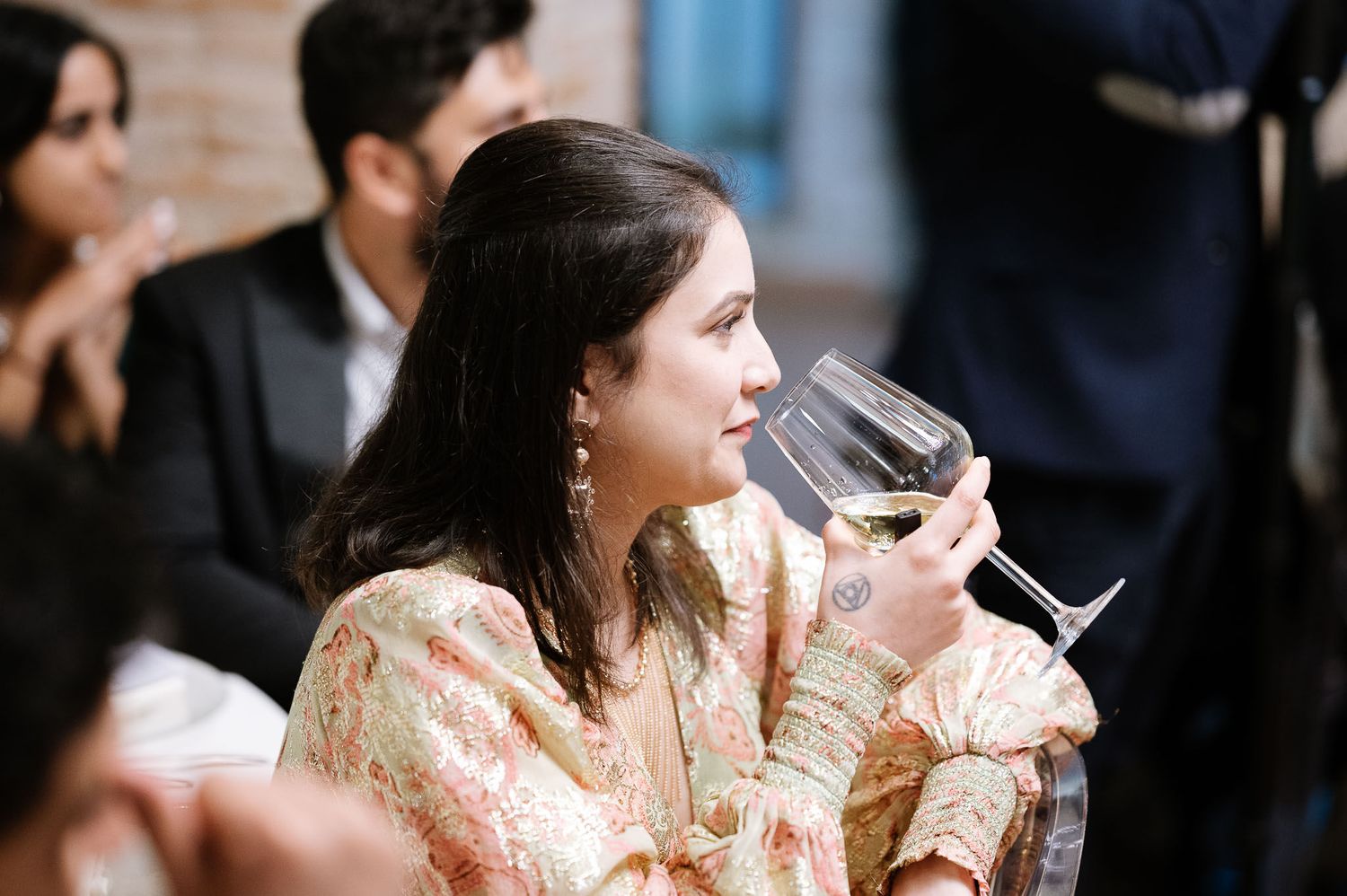 Wedding guest in peach dress enjoying wine during reception celebration.