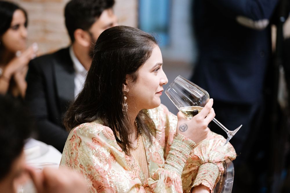 Wedding guest in peach dress enjoying wine during reception celebration.