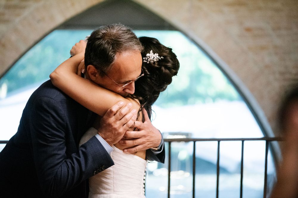 Tender embrace shared during emotional wedding reception moment under stone archway.
