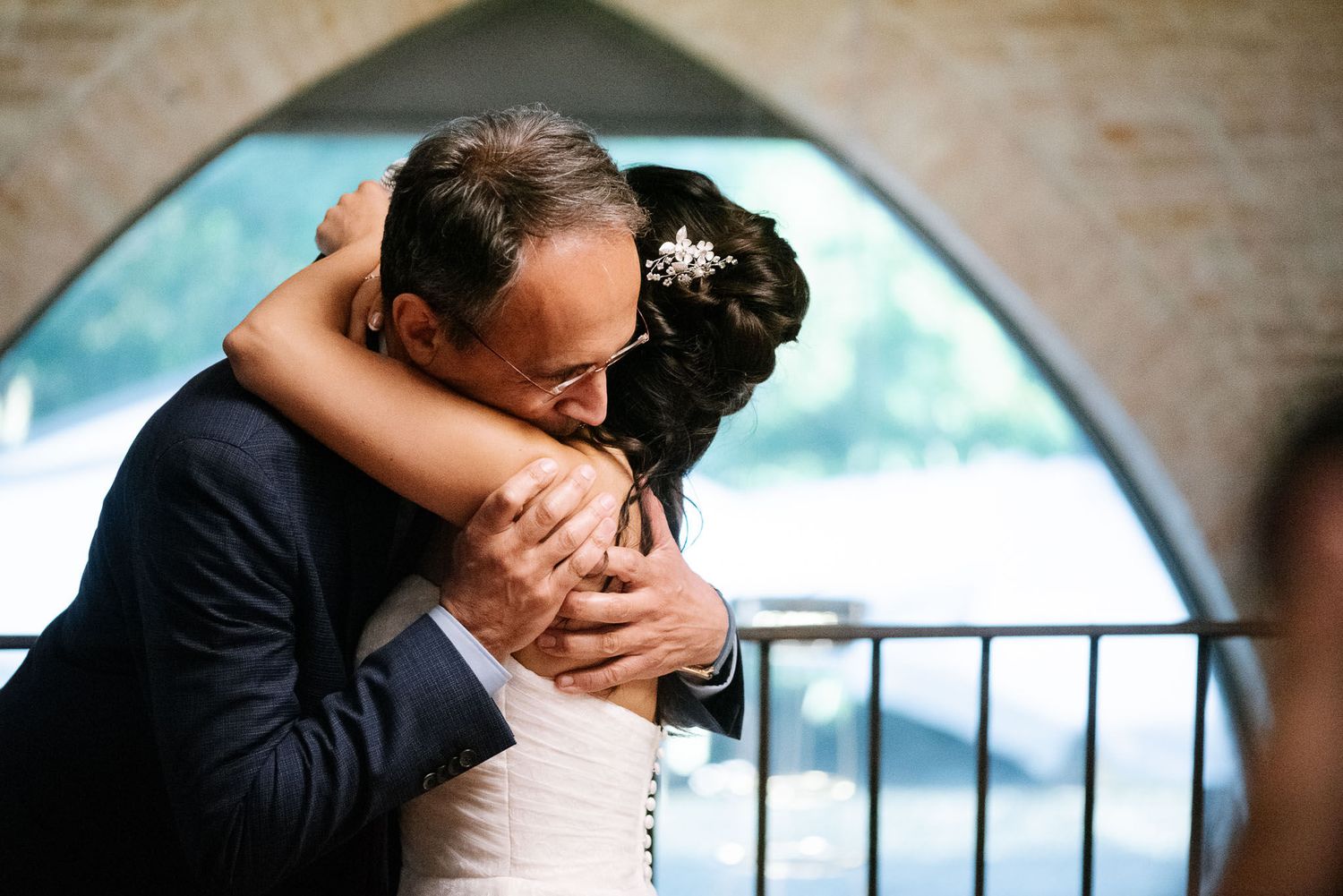 Tender embrace shared during emotional wedding reception moment under stone archway.